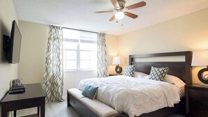 Une chambre à coucher avec un lit, des tables de chevet, un ventilateur de plafond et une fenêtre avec des rideaux.