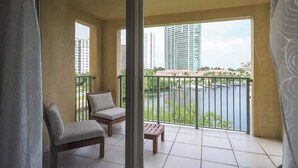 Un balcon avec deux chaises et une petite table, donnant sur une étendue d’eau et des immeubles de grande hauteur.