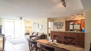 Un coin repas avec une table dressée pour quatre personnes, une cuisine en arrière-plan et un balcon avec vue.