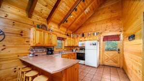 Une cuisine rustique, située dans une cabane en bois, avec un îlot central, des tabourets de bar et les appareils électroménagers de base.