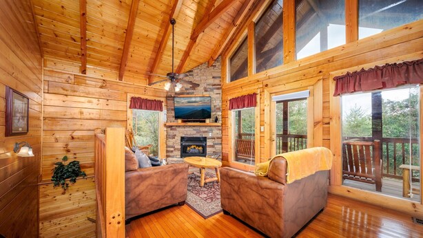 Un intérieur de chalet chaleureux avec des murs en bois, une cheminée, deux canapés en cuir et de grandes fenêtres.
