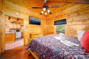 A wooden cabin interior with a bed, a ceiling fan, a kitchen area, and a window with a view. - ERN812 - Eagles Perch-2bd 2.5bth in Pigeon Forge! (Pigeon Forge)