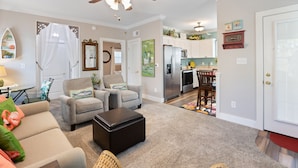 A living room with a ceiling fan, two armchairs, a coffee table, and a dining area with a kitchen in the background.