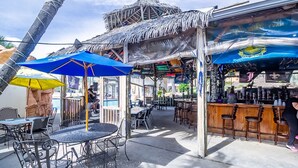 An outdoor bar area with tiki-style umbrellas, metal chairs, and a bar counter.