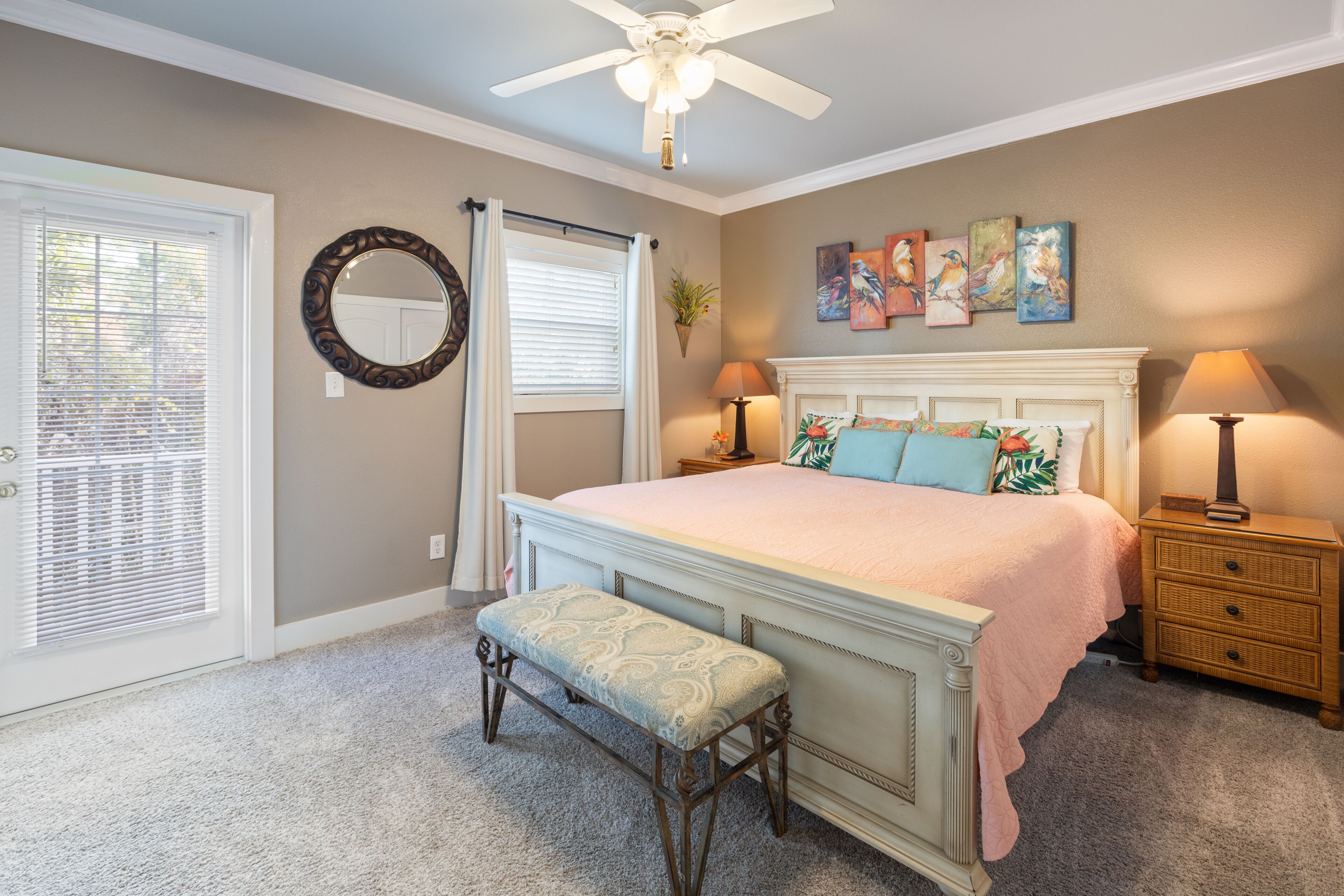 A bedroom with a bed, bench, bedside tables, a ceiling fan, and artwork on the wall.