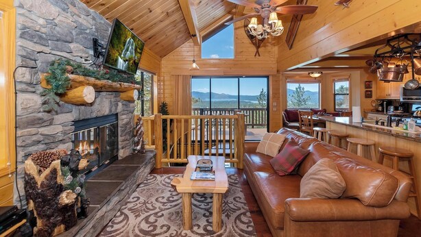 A cozy cabin interior with a stone fireplace, a wooden ceiling, a leather sofa, and a dining area.