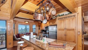 A wooden cabin kitchen with a granite countertop, hanging copper pots, and a large refrigerator.