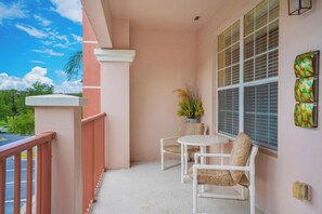 Ein Balkon mit weißer Brüstung, zwei Stühle, ein kleiner Tisch und ein Blumentopf.