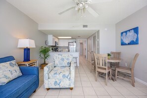 A living room with a blue sofa, a patterned armchair, and a dining area with wooden chairs and a table.