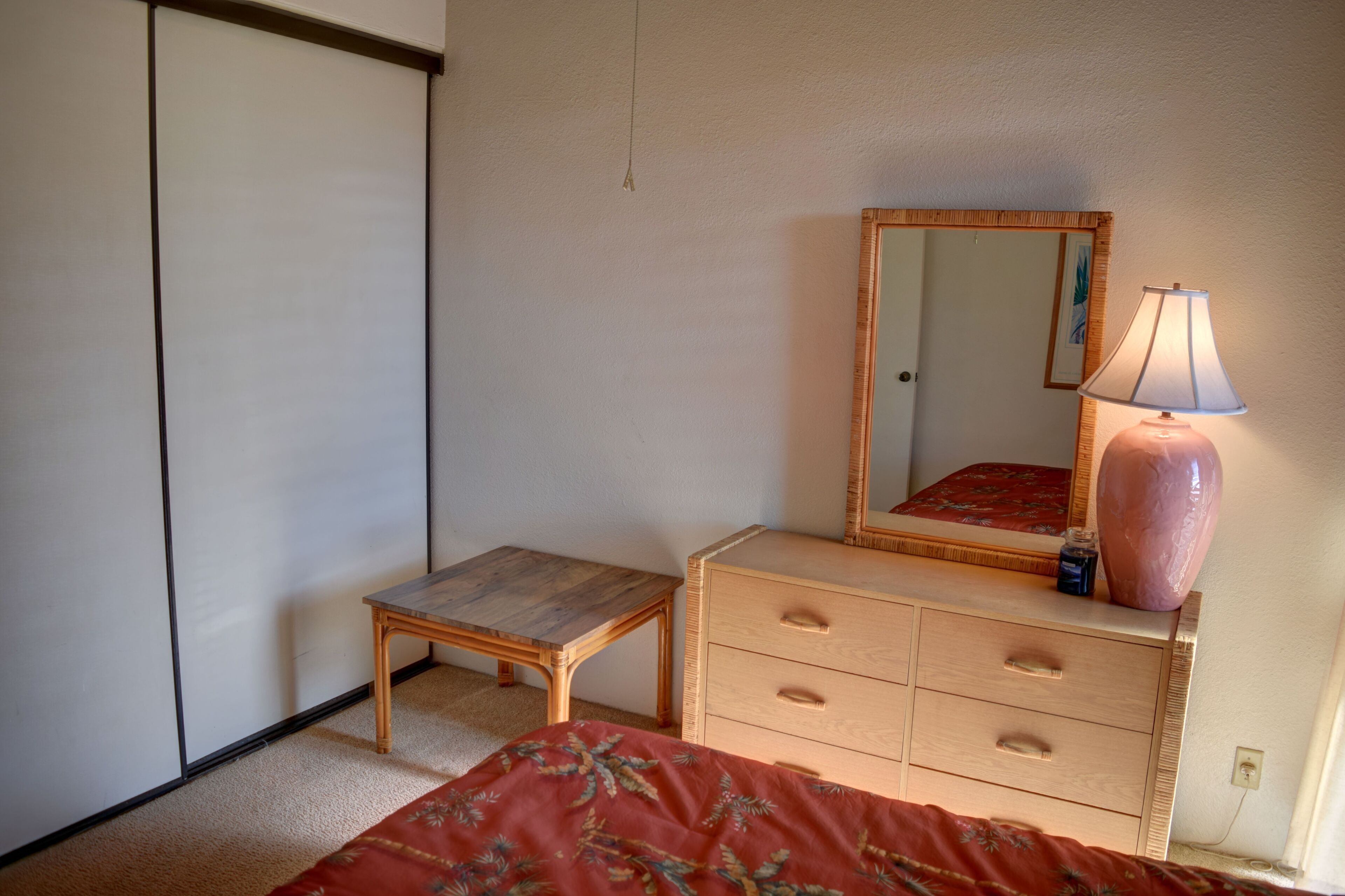 Un dormitorio con cama, mesita de noche de madera, cómoda, espejo y lámpara.