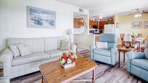 A living room with a sofa, armchairs, a coffee table with flowers, a dining area with a table and chairs, and a kitchen in the background. - B527 at The Myrtle Beach Resort (Myrtle Beach)