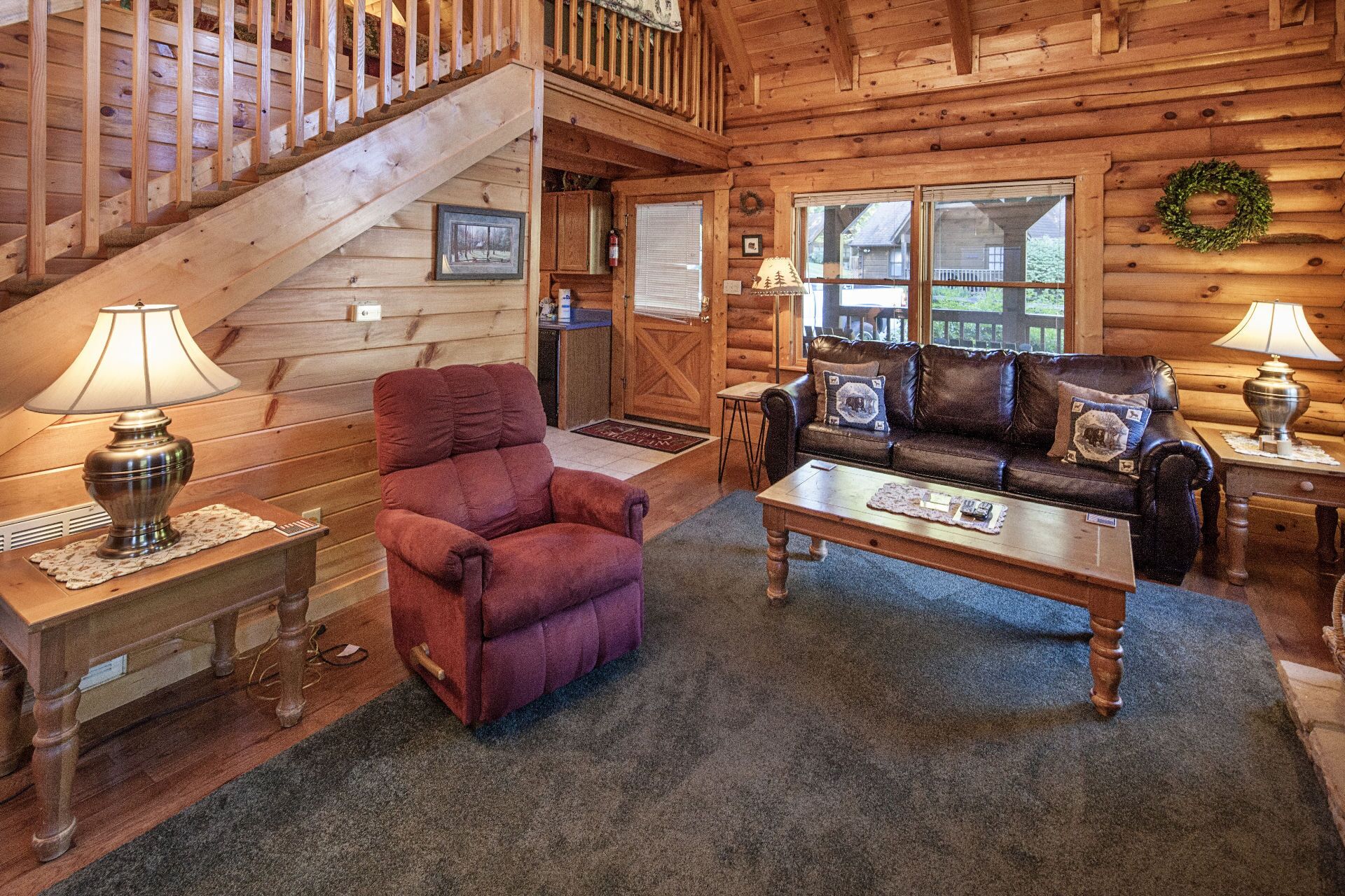 L’intérieur d’un chalet confortable, avec un escalier, un canapé en cuir, un fauteuil rouge et une table basse en bois.