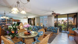 A spacious living room with wicker furniture, a glass-top dining table, and a balcony with a view. - Top-Floor Kamaole Sands Condo – Vaulted Ceilings, A/C, Lanai, Walk to Beach! (Kihei)