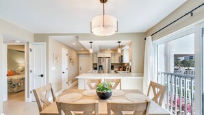 Een moderne keuken met een centraal eiland, een eethoek met een tafel en stoelen, en een groot raam met toegang tot een balkon.