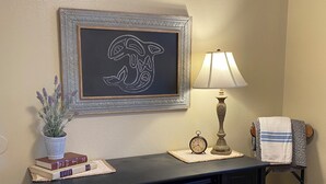A neatly arranged desk with a framed artwork, a potted plant, a lamp, and a towel on a chair.