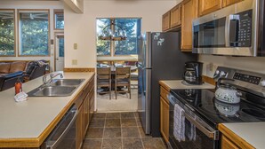 A modern kitchen with a stainless steel refrigerator, a microwave, and an oven. There is a dining area with a table and chairs visible through a doorway. - Beautiful home w/fireplace, amazing views & community hot tub - Hidden Village Cozy Getaway (Gallatin Gateway)