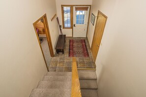 A staircase with a wooden handrail, a red patterned rug, and a door with a window.