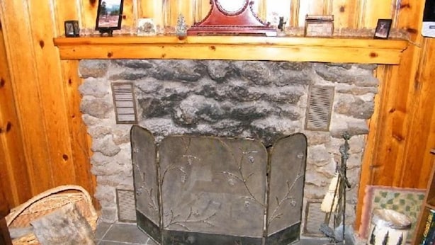 A stone fireplace with a decorative screen, a wooden mantel with framed pictures, and a rug on the floor. - Honeymoon Cozy Forest Cabin (Greer)