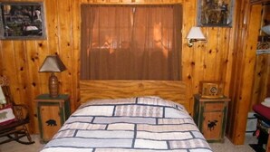 A wooden room with a bed, a lamp, and a small cabinet. - Honeymoon Cozy Forest Cabin (Greer)