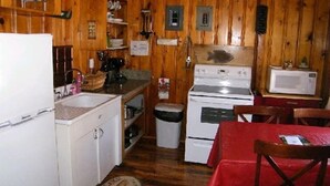 A compact kitchen with wooden walls, a white refrigerator, a stove, a microwave, and a sink. - Honeymoon Cozy Forest Cabin (Greer)