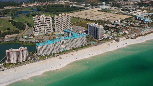 Vista aérea de una zona turística costera con múltiples hoteles de gran altura, una playa de arena y un puerto deportivo.