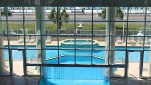 Vista de una piscina con jacuzzi, rodeada por una valla y con amplia vista al océano a través de grandes ventanales.