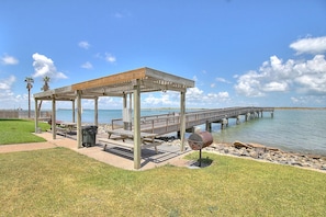A wooden gazebo with benches, a barbecue grill, and a view of a pier extending into a body of water.
