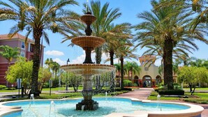 A multi-tiered fountain surrounded by palm trees and a building with arched windows. - Orlando getaway with all the comforts of home! (Orlando)