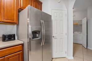 Eine Küche mit einem Edelstahl-Kühlschrank, Holzschränken, einer weißen Tür und einem Waschbereich im Hintergrund.
