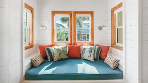 A cozy seating area with a bench and cushions, large windows with wooden frames, and a view of greenery outside. - Tropical home has 3 comfortable bedrooms and 3 full baths. Screened in porch! Ch (Port Aransas)