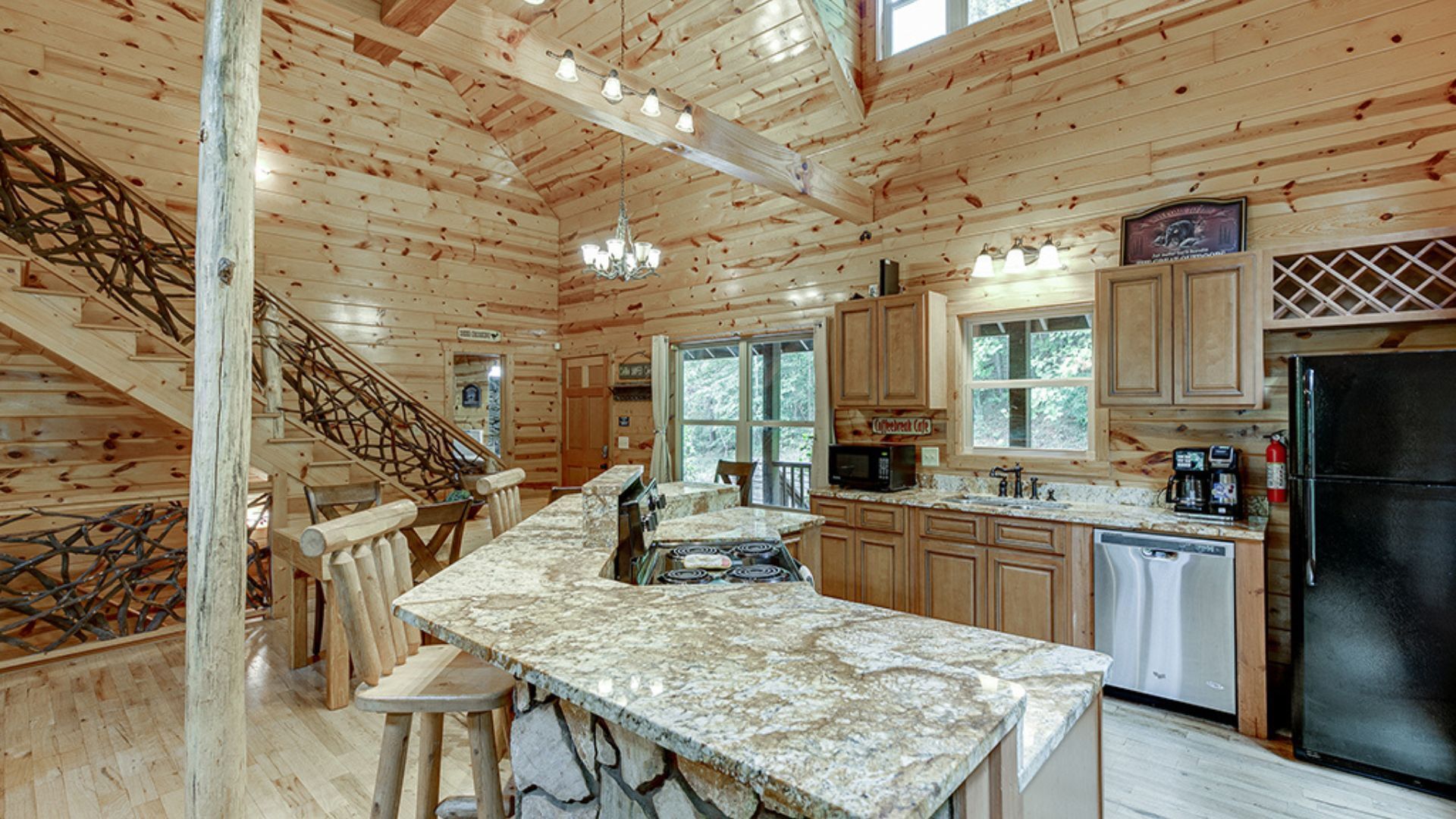 Interior de una cabaña de madera con cocina, comedor y una escalera.
