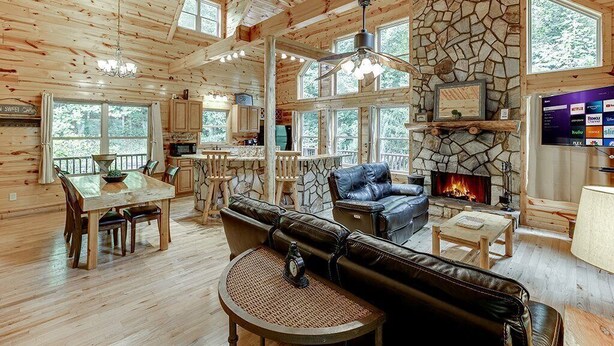L’intérieur d’une cabane en rondins, avec une cheminée en pierre, un coin repas en bois et un espace salon confortable.