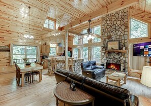 A log cabin interior with a stone fireplace, wooden dining area, and a cozy seating area.