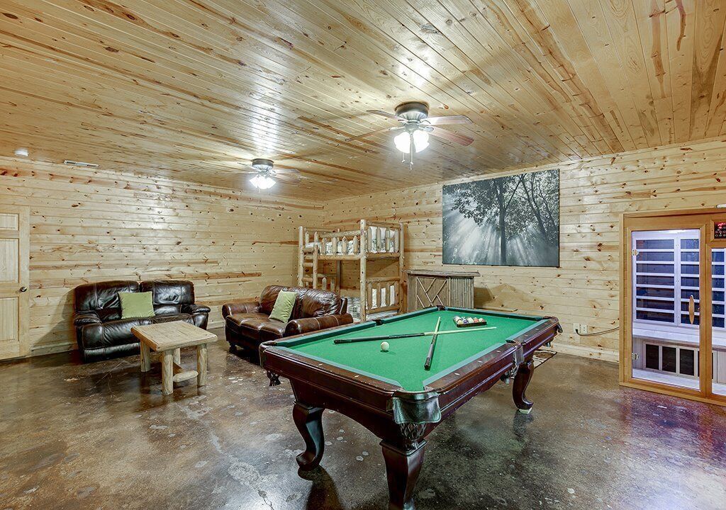 A wooden-paneled room with a pool table, leather sofas, and a ceiling fan.
