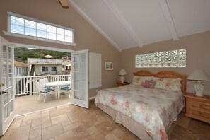A bedroom with a large bed, a nightstand, a window with decorative shutters, and an open door leading to a balcony with a table and chairs. - 329D: Beautifully Decorated Two-Story Home, Spacious Deck, Fireplace, WIFI, BBQ (Avalon)