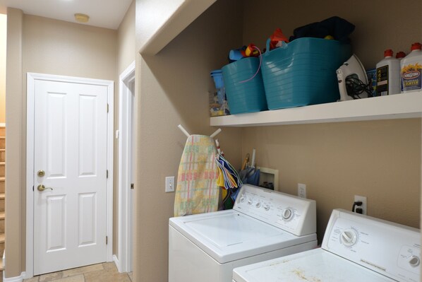 A laundry area with two white washers and dryers, a shelf with cleaning supplies, and a door leading to another room. - 329D: Beautifully Decorated Two-Story Home, Spacious Deck, Fireplace, WIFI, BBQ (Avalon)