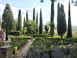 Un jardín con setos bien cuidados, altos cipreses y una variedad de plantas en flor.