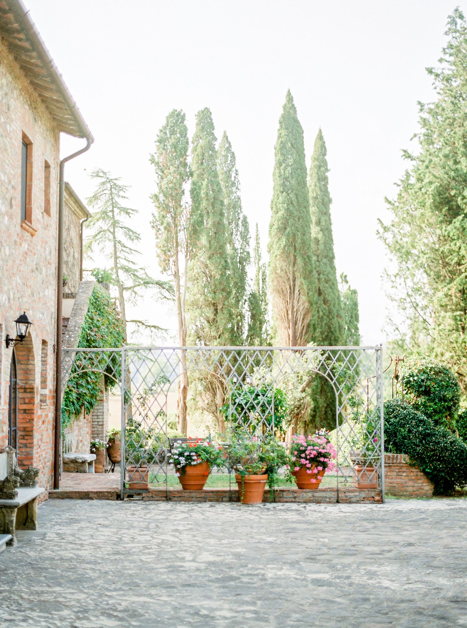 A courtyard with a stone building, a metal fence, and potted plants.