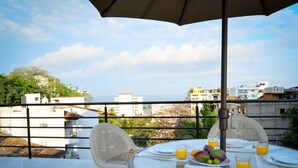 Una mesa dispuesta para el desayuno, con fruta y zumo de naranja, con vistas a un paisaje urbano.