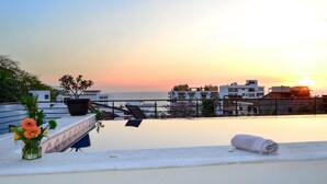 Terraza en la azotea con vista al atardecer sobre el mar, una planta en maceta y una toalla enrollada.