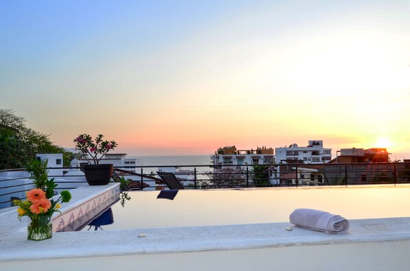 A rooftop terrace with a view of the sunset over the sea, a potted plant, and a rolled towel.