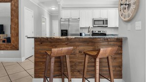A modern kitchen with white cabinets, stainless steel appliances, and wooden stools.