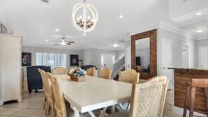 A spacious dining area with a large table and wicker chairs, a chandelier, and a wooden accent wall.