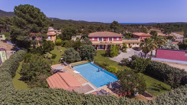 A hotel with a swimming pool, surrounded by lush greenery and a hilly landscape.
