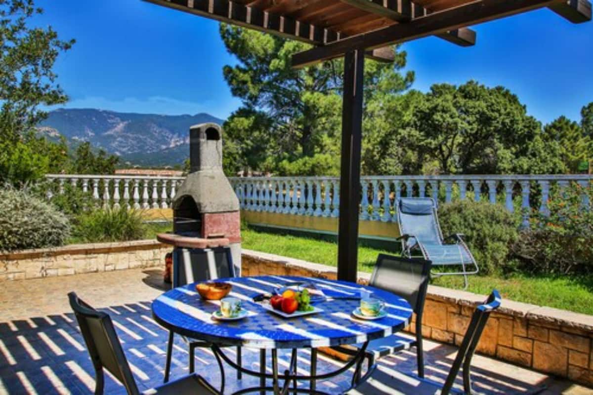 Une terrasse extérieure avec une table ronde, des chaises et un barbecue.