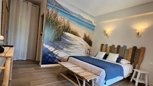 Een slaapkamer met een bed, nachtkastjes, een bankje, een schilderij van een strand en twee wandlampen.