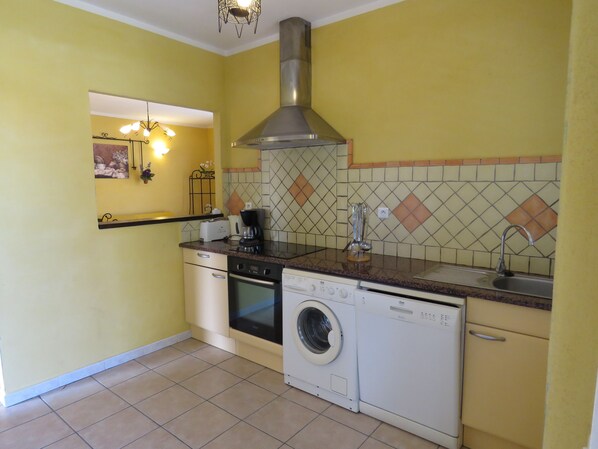 A compact kitchen with a washing machine, oven, and a coffee maker on the countertop.