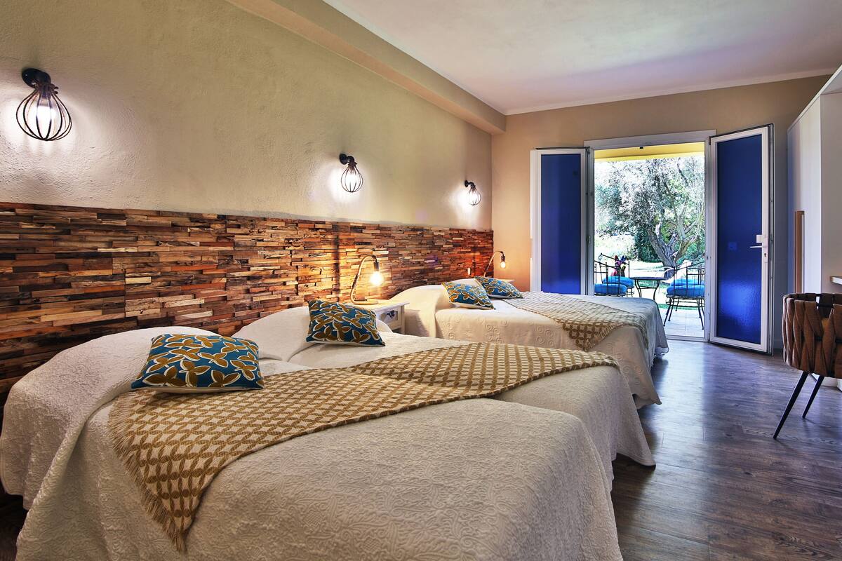 Une chambre d’hôtel avec deux lits, une tête de lit en bois et un balcon avec des chaises.