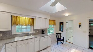 A kitchen with white cabinets, a granite countertop, a built-in dishwasher, and a window with yellow curtains. - Grace Cottage 3 bedrooms, 2 bathrooms (Jekyll Island)