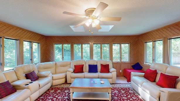 A spacious living room with a ceiling fan, large windows, and a red patterned rug. - Grace Cottage 3 bedrooms, 2 bathrooms (Jekyll Island)